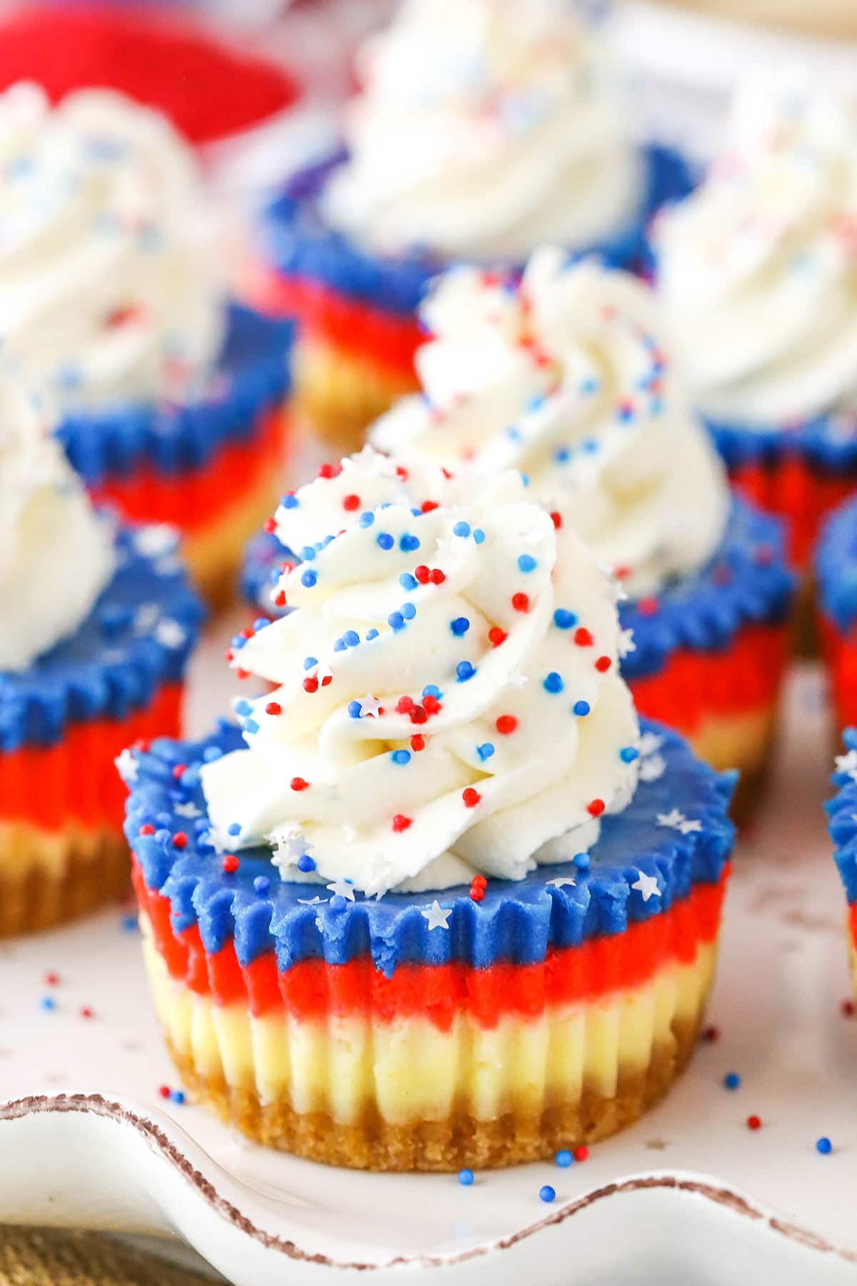 These Red, White and Blue Mini Cheesecakes are smooth, creamy and easy to make! Perfect for your patriotic celebration! Red White and Blue Mini Cheesecakes on a white platter