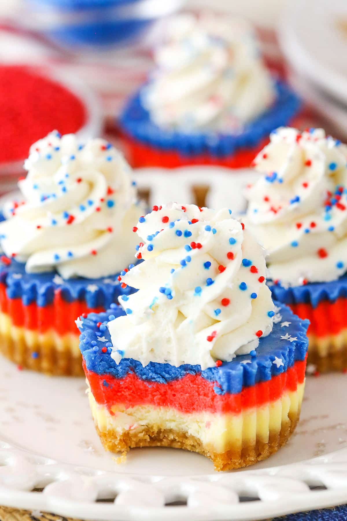 These Red, White and Blue Mini Cheesecakes are smooth, creamy and easy to make! Perfect for your patriotic celebration! A Red White and Blue Mini Cheesecake with a bite removed on a white plate