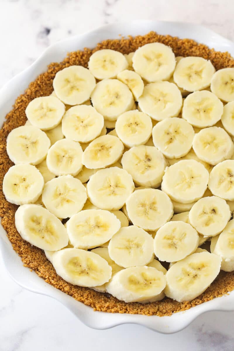 Banoffee Pie is an irresistible dessert made with a graham cracker crust, toffee filling, banana slices, and whipped cream. Banana slices on top of toffee filling in a graham cracker crust