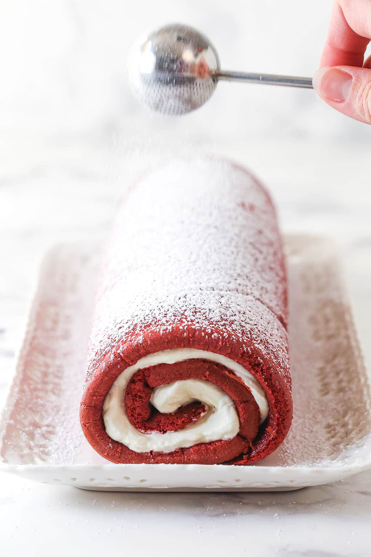 This red velvet cake roll is light and tender with the signature tang and hint of chocolate flavor. Perfect for Christmas & Valentine's Day! Red velvet cake roll on a platter