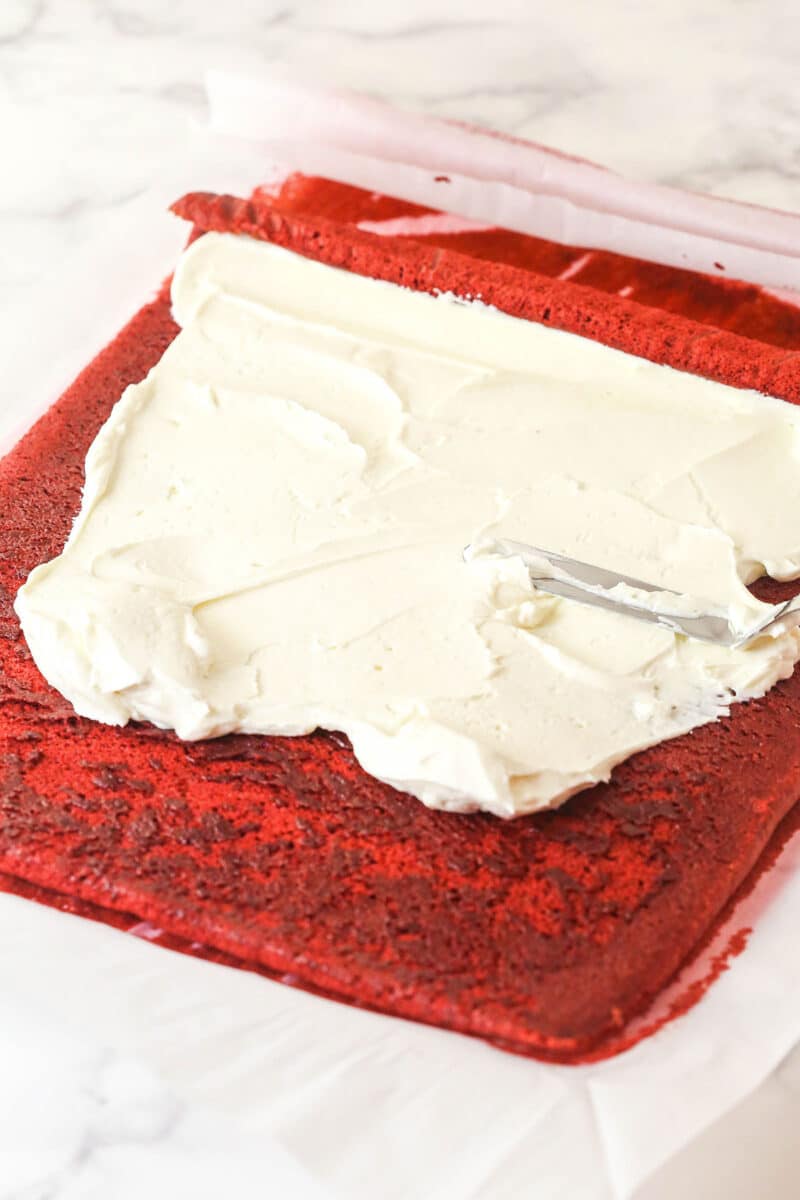 This red velvet cake roll is light and tender with the signature tang and hint of chocolate flavor. Perfect for Christmas & Valentine's Day! Cream cheese whipped cream spread on red velvet cake