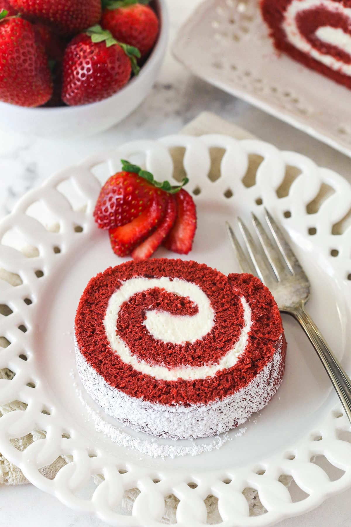 This red velvet cake roll is light and tender with the signature tang and hint of chocolate flavor. Perfect for Christmas & Valentine's Day! Overhead view of a slice of red velvet cake roll on a white plate