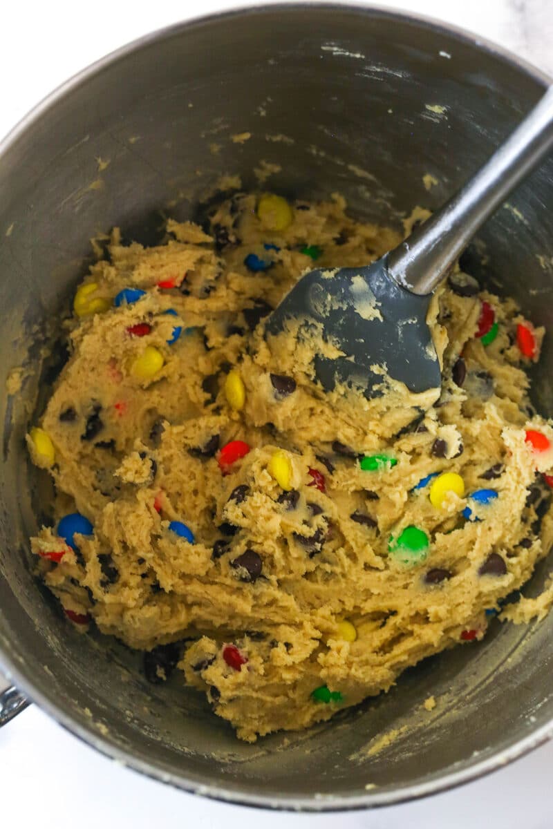 Folding chocolate chips and M&Ms into cookie dough for M&M cookie recipe.