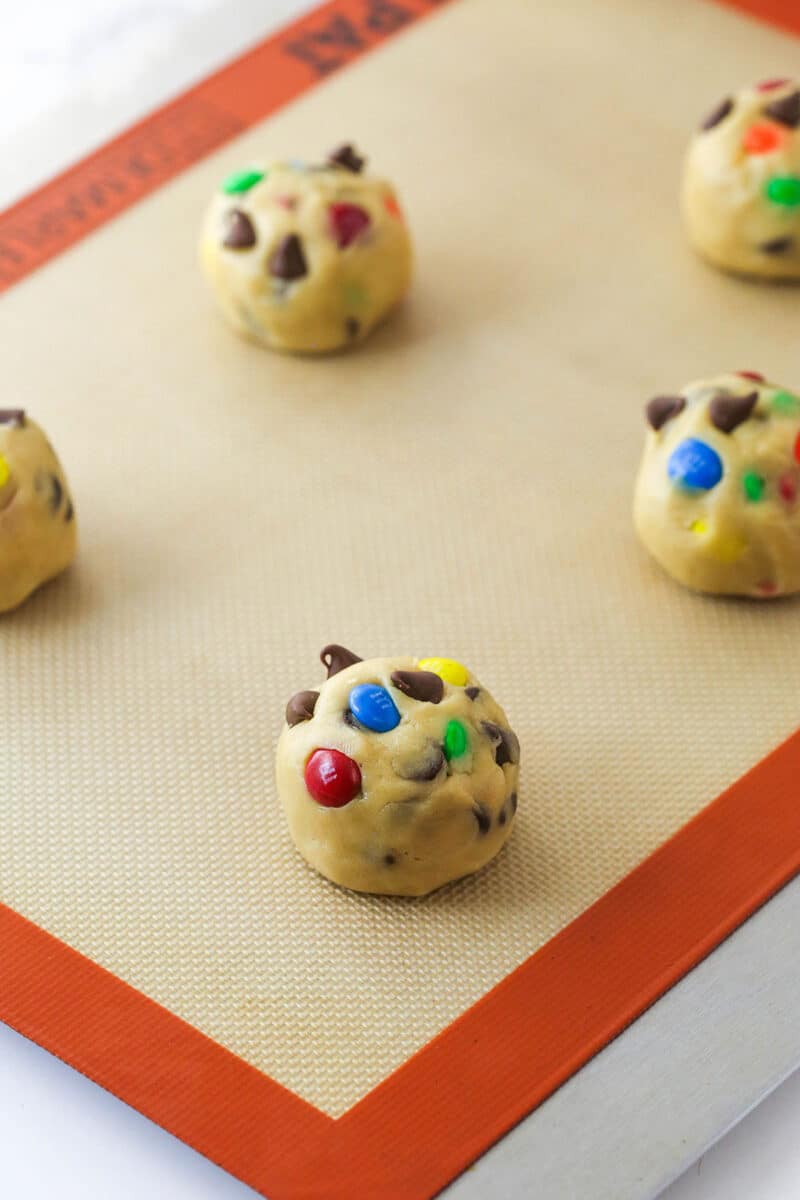 Balls of M&M cookie dough on a baking sheet ready to be baked.