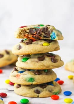 A stack of M&M cookies. The top cookie has a bite taken out of it.
