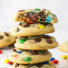 A stack of M&M cookies. The top cookie has a bite taken out of it.
