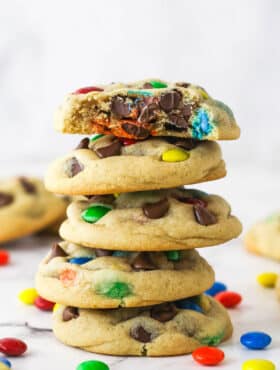 A stack of M&M cookies. The top cookie has a bite taken out of it.