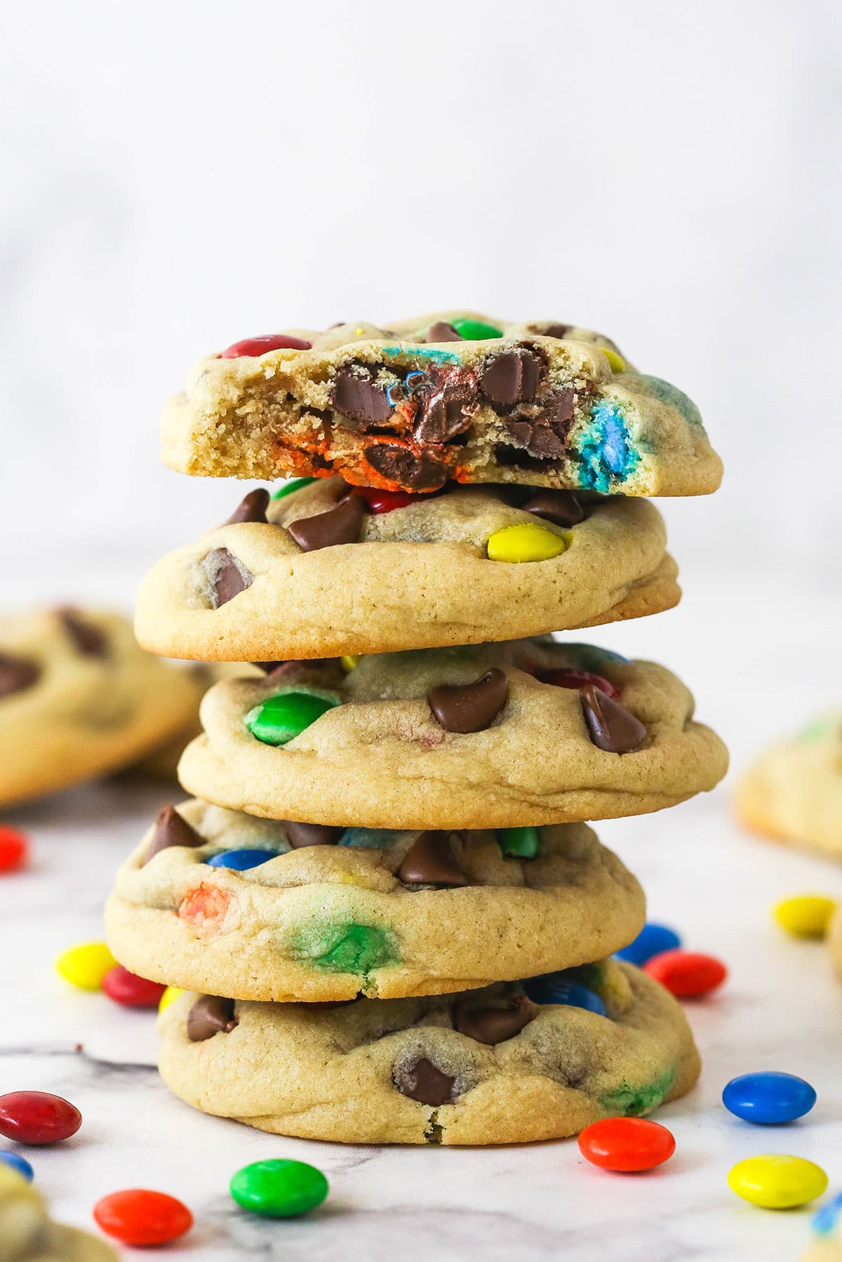You've got to make this M&M Cookie Recipe right now! The cookies are thick, chewy, pillowy-soft, and loaded with colorful chocolaty goodness. A stack of M&M cookies. The top cookie has a bite taken out of it.