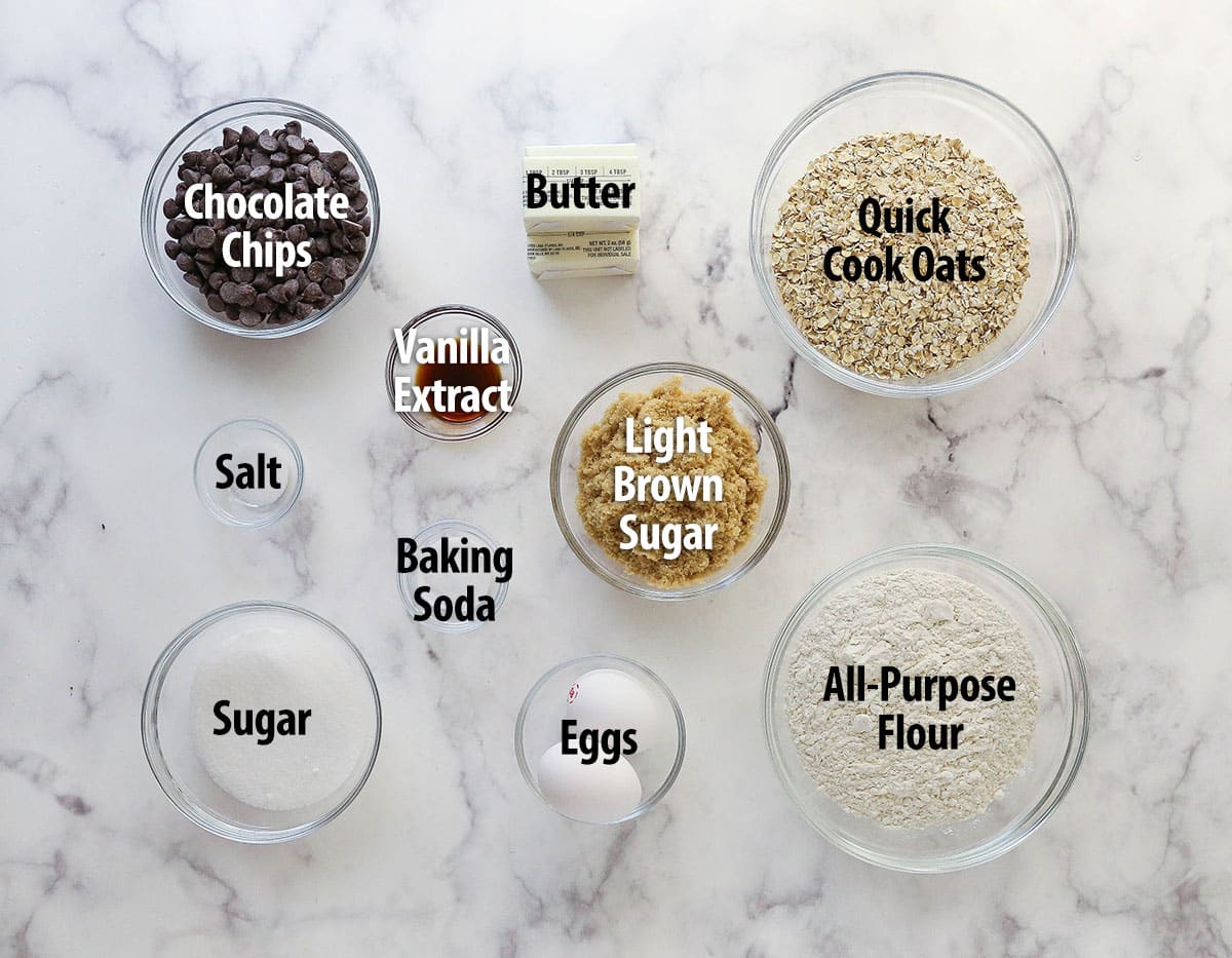 Ingredients for oatmeal chocolate chip cookies labeled on a work surface.