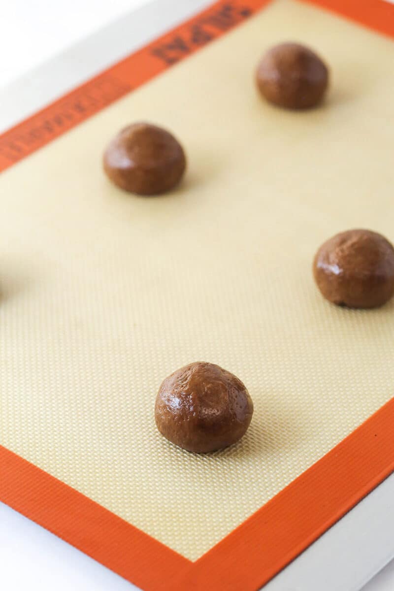 Balls of cookie dough on baking sheet with silicone baking mat