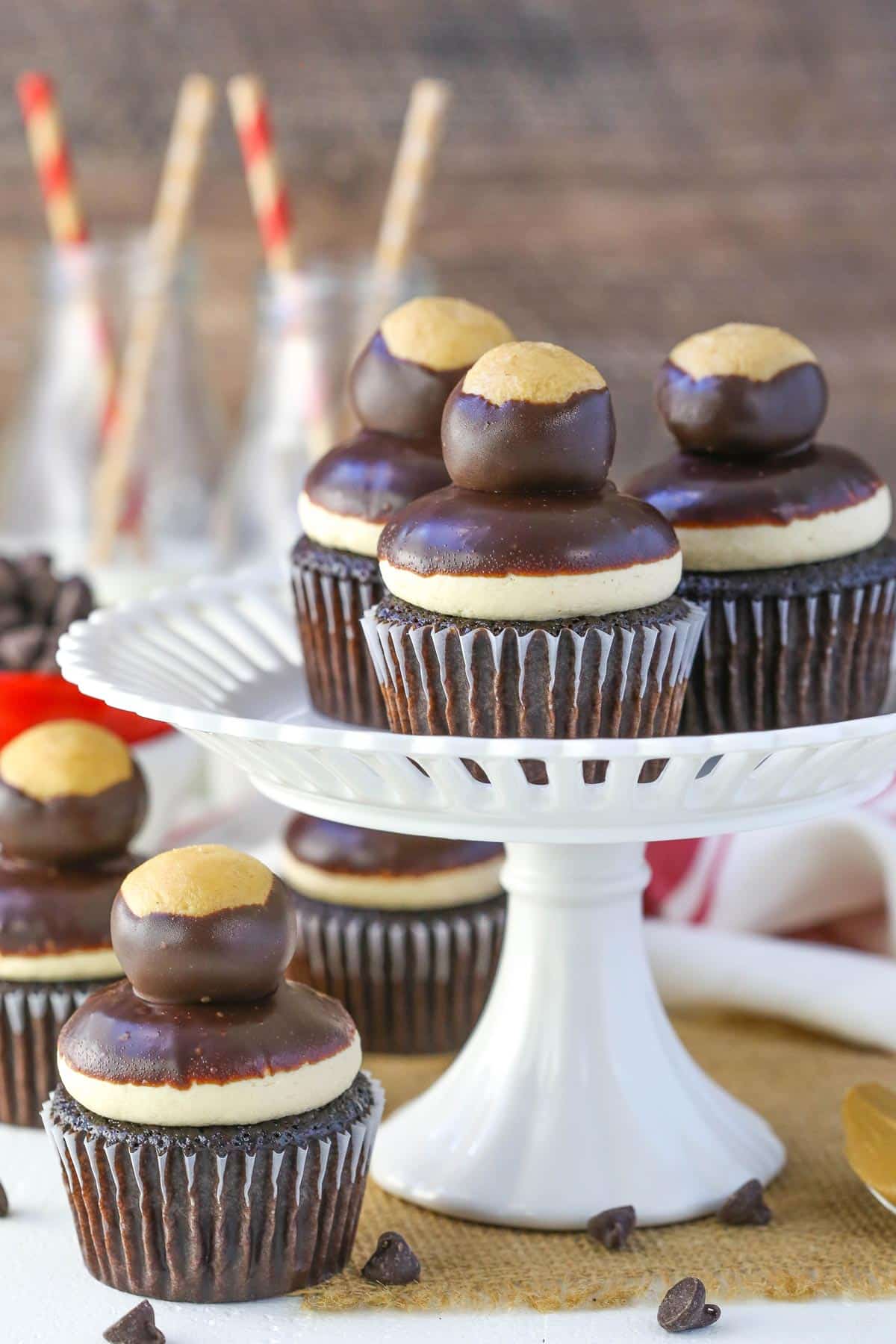 Three peanut butter chocolate buckeye cupcakes on a white cake platter with more cupcakes below the patter.