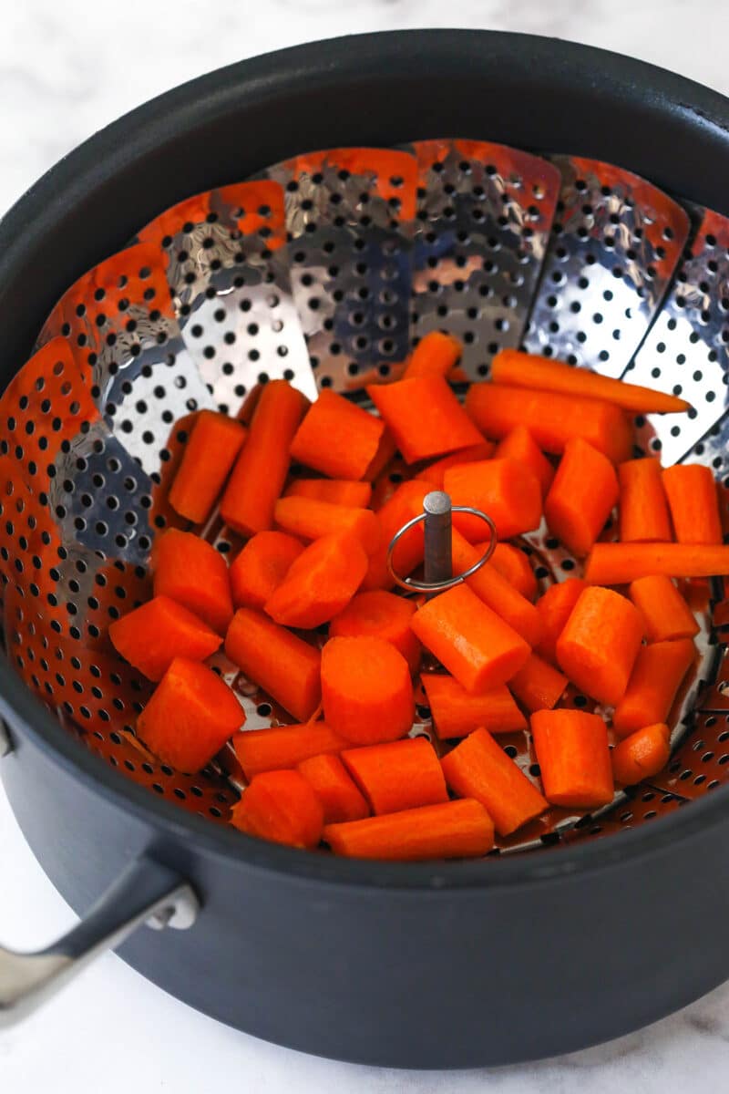 Steaming chunks of carrots in a steamer basket set over boiling water.