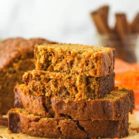 Slices of carrot cake loaf stacked on top of each other. The top slice is broken in half.