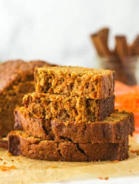 Slices of carrot cake loaf stacked on top of each other. The top slice is broken in half.