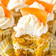 An unwrapped carrot cake cheesecake cupcake with a bite taken out of it.