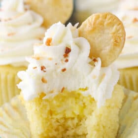 An unwrapped coconut cream pie cupcake with a bite taken out of it to show filling.