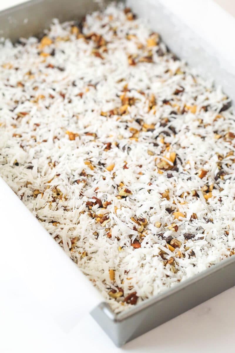 Scattering pecans and shredded coconut over a graham cracker crust topped with chocolate and butterscotch chips.
