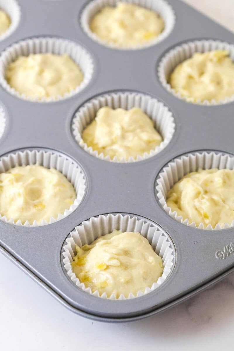Pineapple cupcake batter in cupcake liners in a cupcake pan.