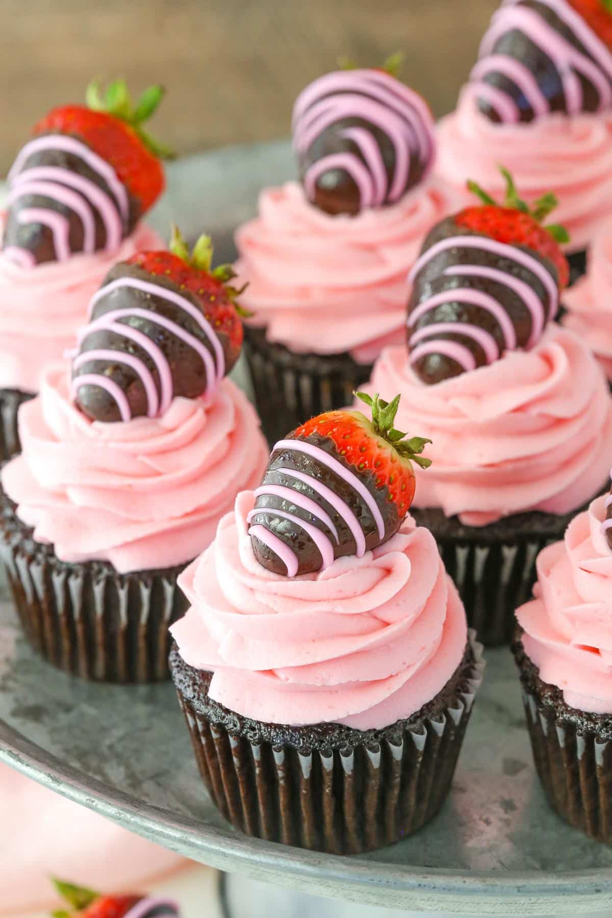 Several chocolate covered strawberry cupcakes on a silver cake plate.