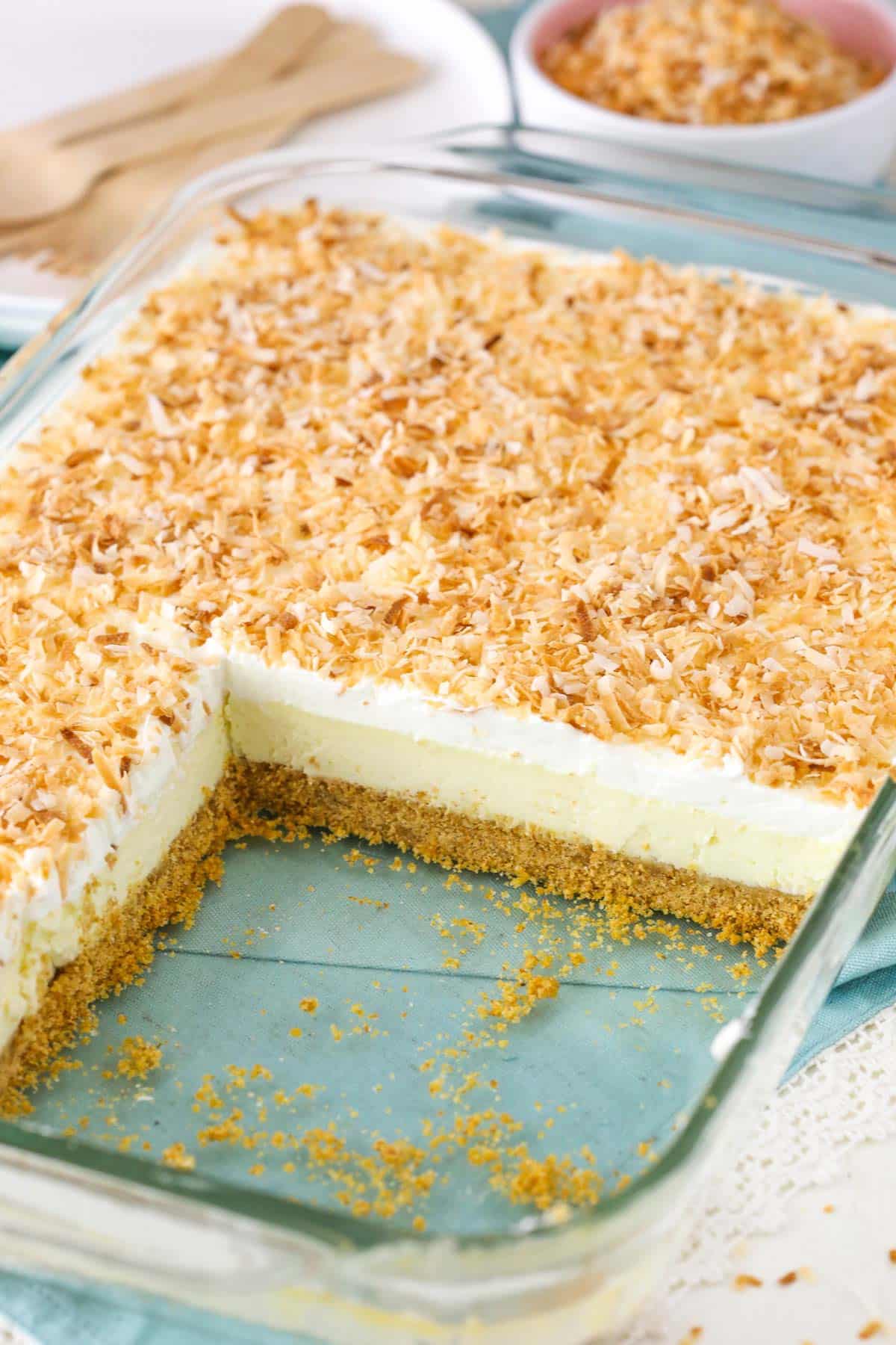 A pan of easy coconut cheesecake with several portions removed to show layers.