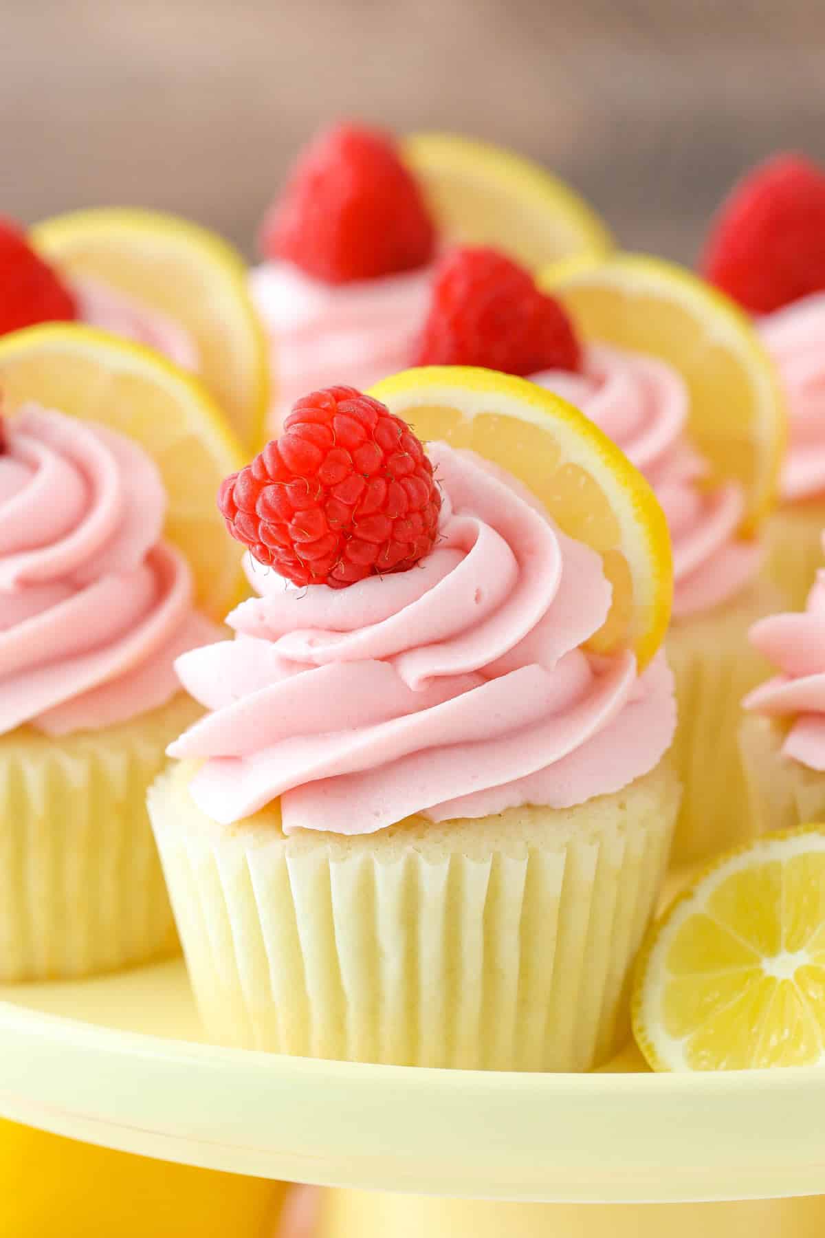 Close up of a lemon raspberry cupcake on a yellow cake plate.
