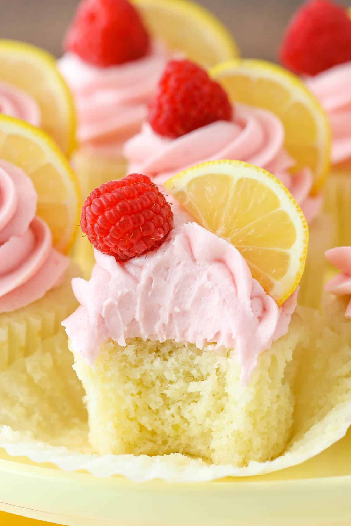 A lemon raspberry cupcake with a bite taken out of it.