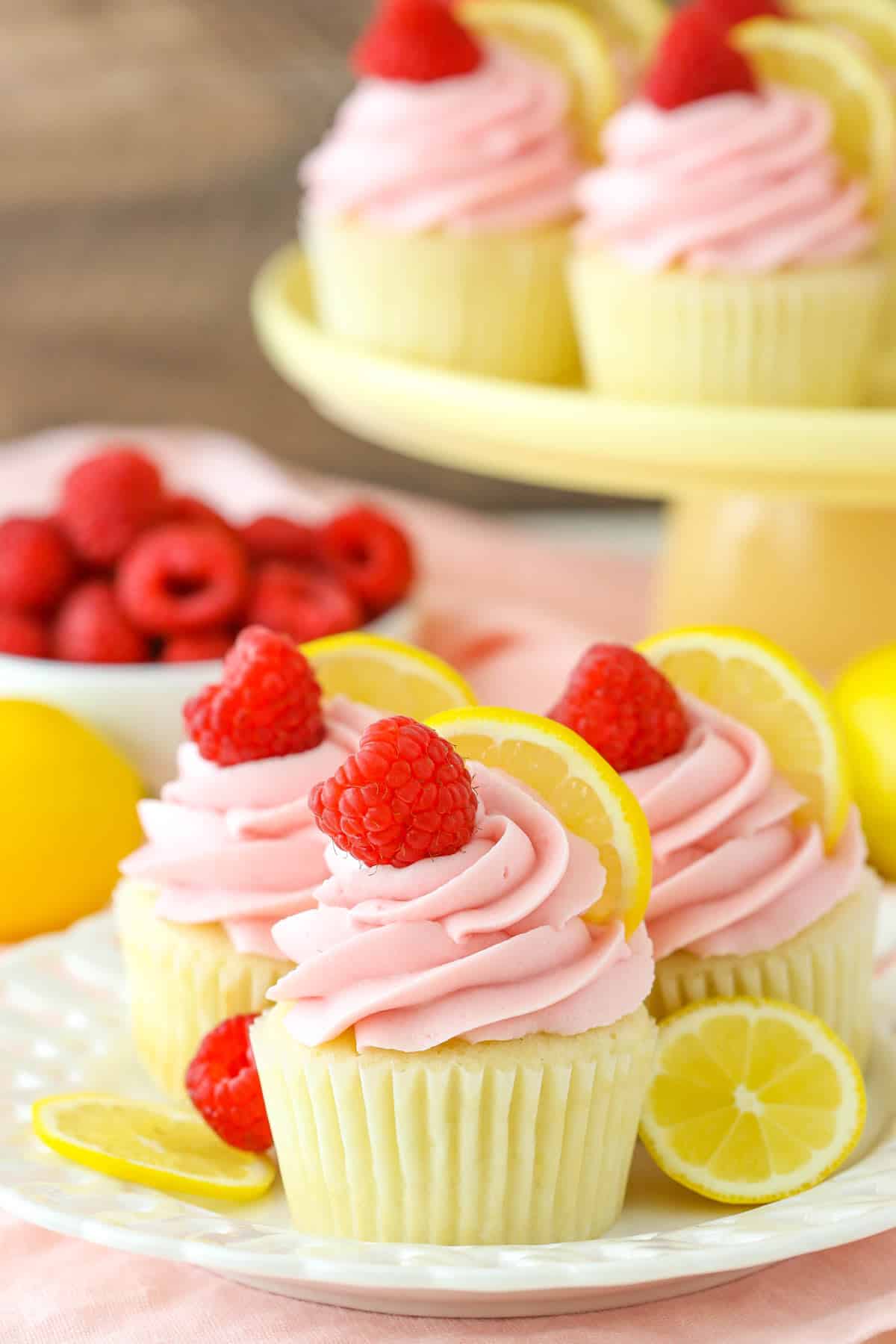 Side view of three lemon raspberry cupcakes on a small white dessert plate with more cupcakes in the background.