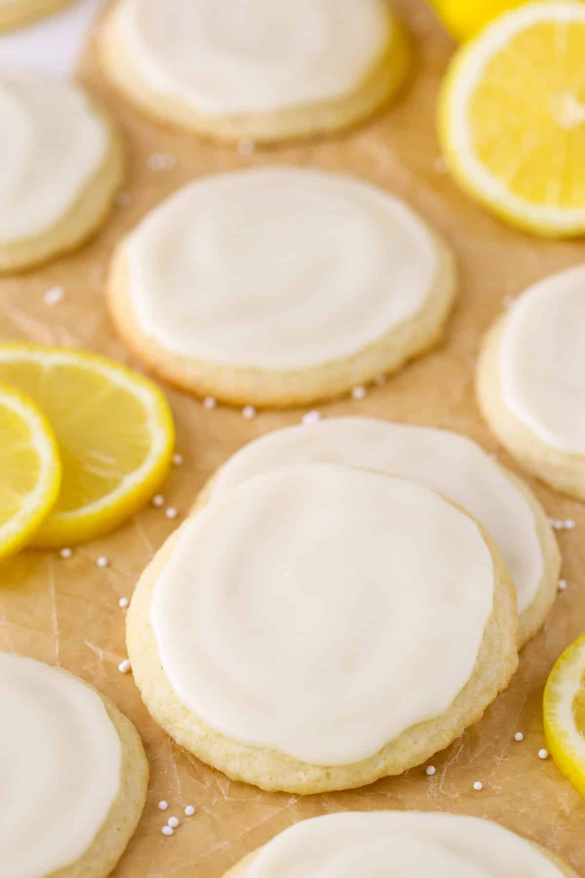 Close up of two Limoncello Cookies stacked on each other and surrounded by more cookies and lemon slices.