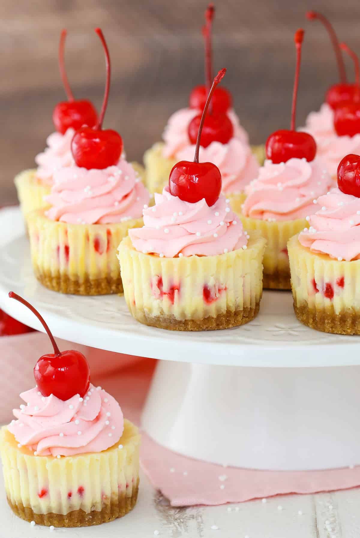 Mini cherry almond cheesecakes on a white cake plate with one cake below the platter.