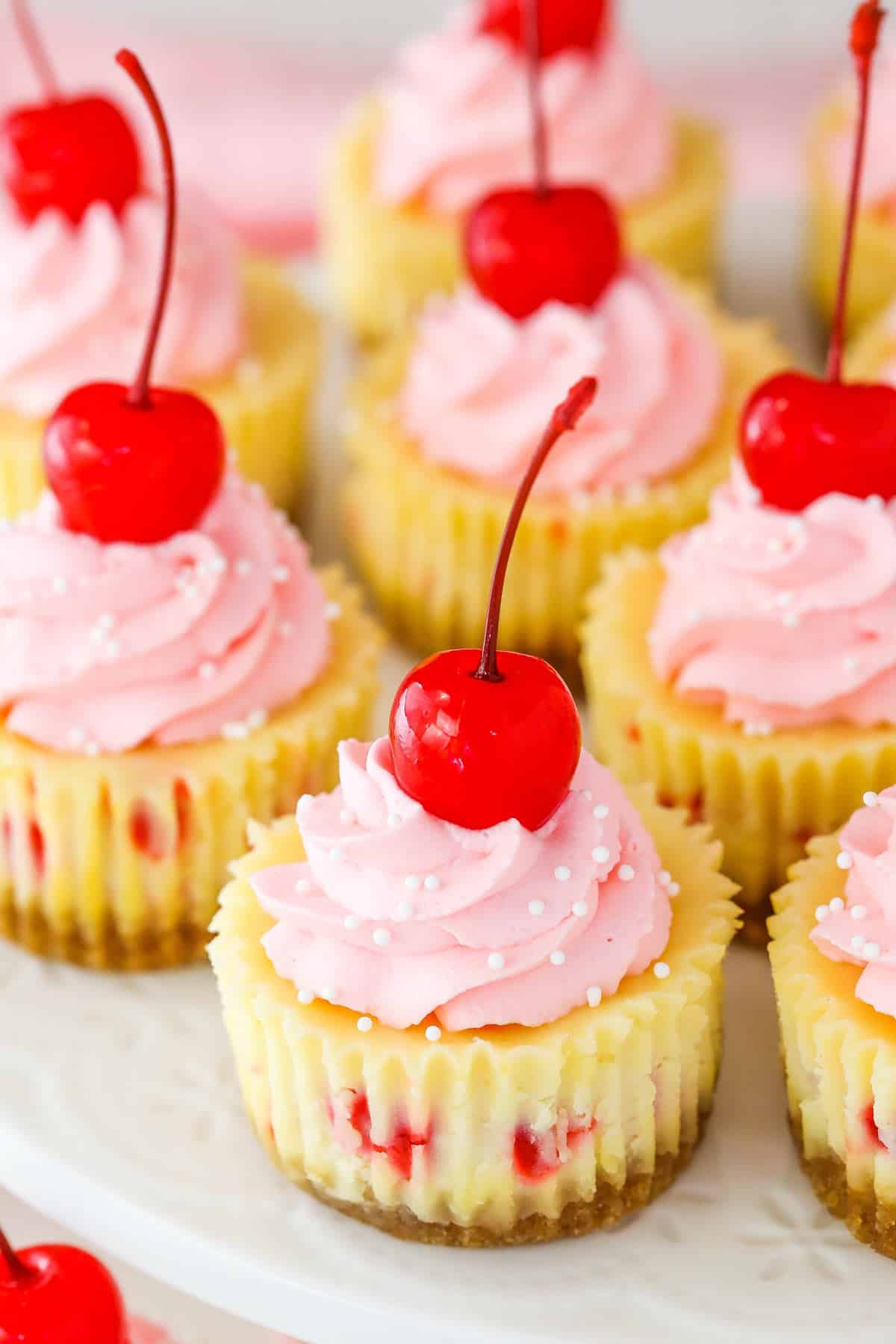Several mini cherry almond cheesecakes on a white platter.