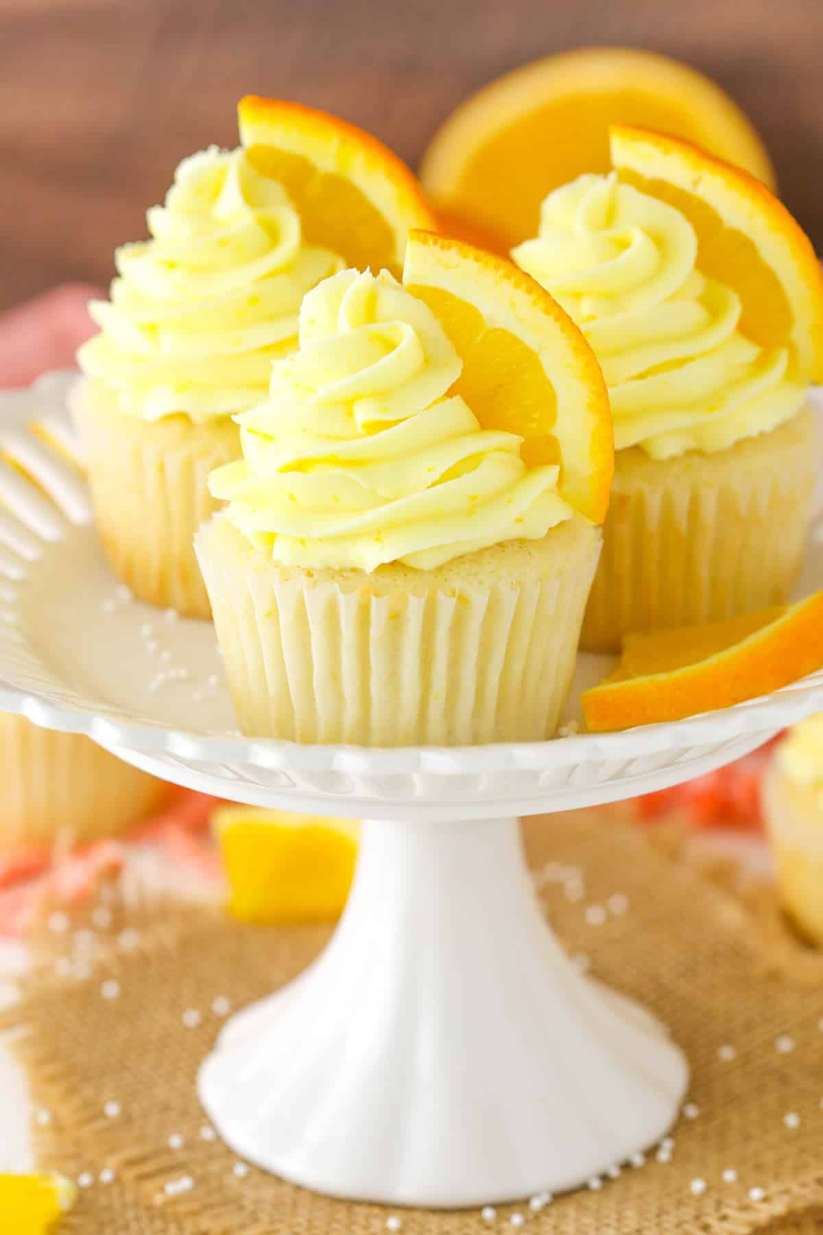 Three orange cream cupcakes on a small white cake plate.