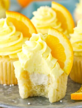 An orange cream cupcake with a bite taken out of it.