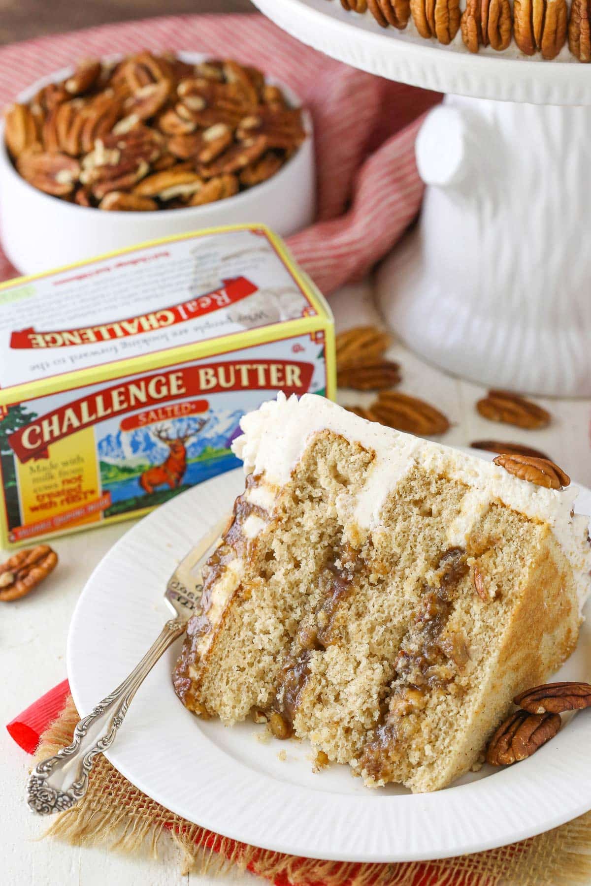 A slice of pecan pie layer cake on a white plate by a box of butter.
