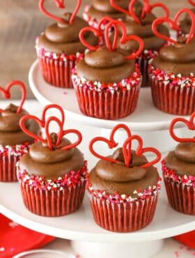 Close up of several rows of red velvet cupcakes on a white tiered cake plate.
