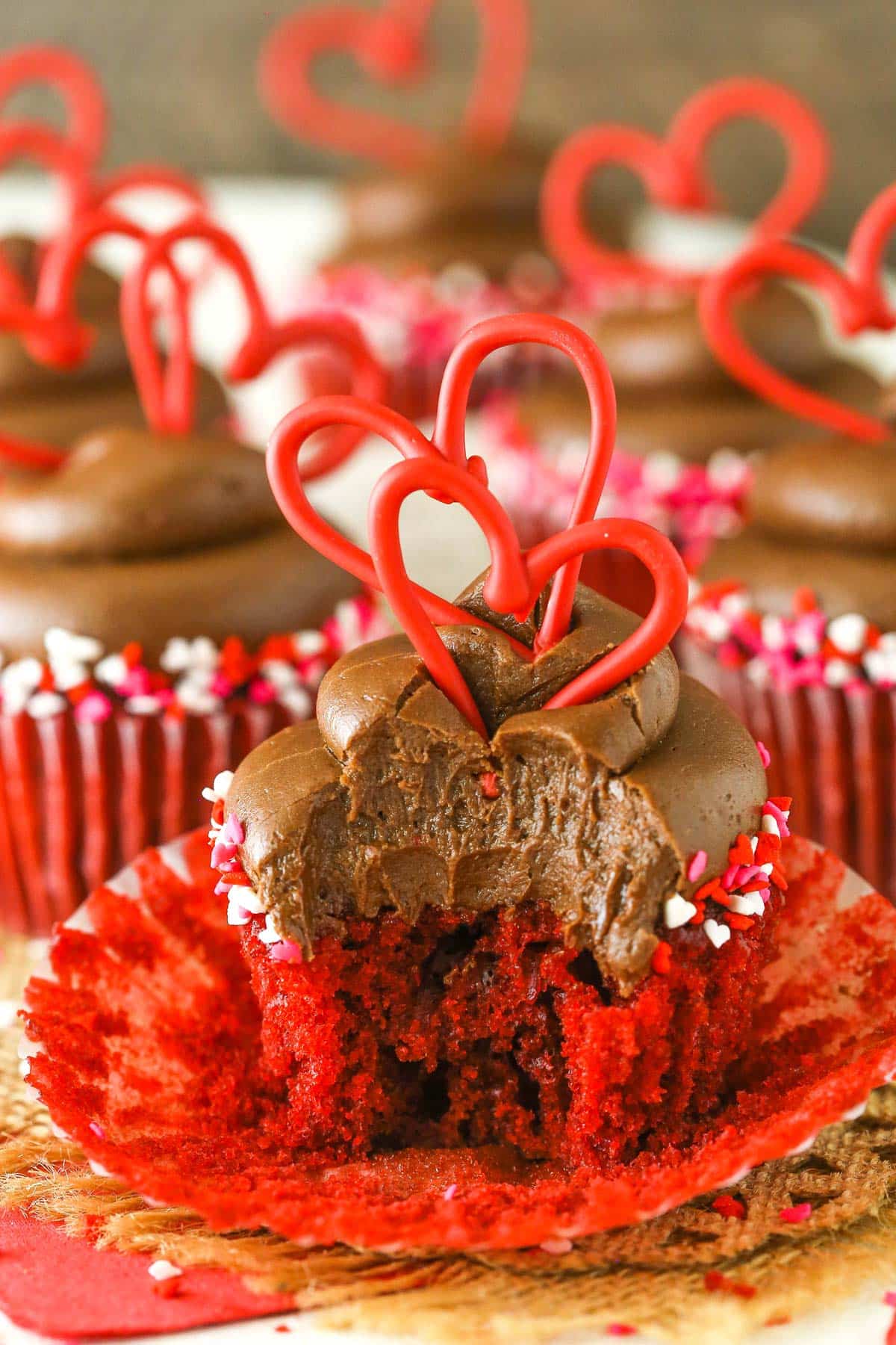 A red velvet cupcake sitting on its wrapper with a large bite taken out of it.