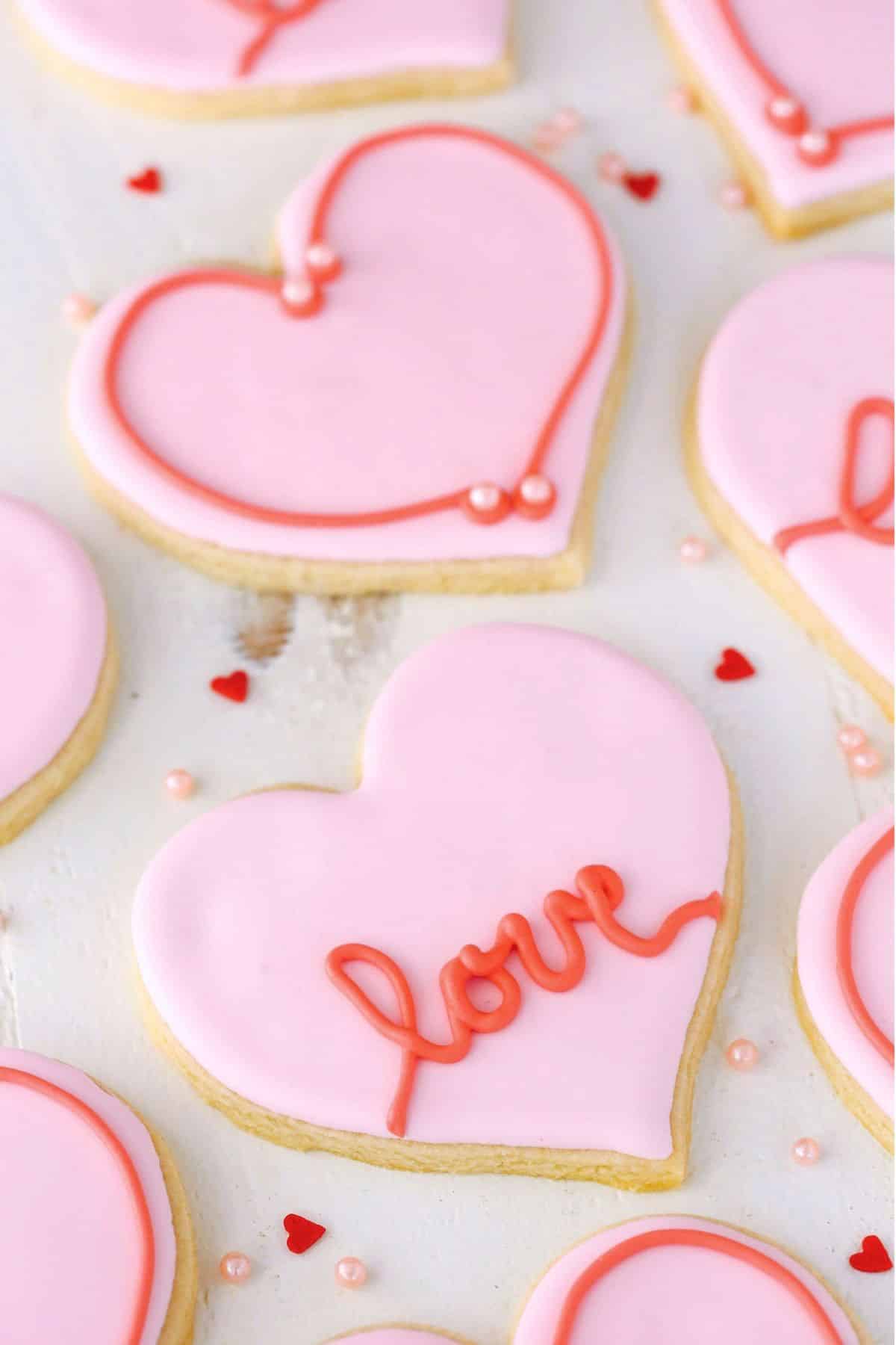 Heart-shaped cutout cookies surrounded by sprinkles drying on the counter.