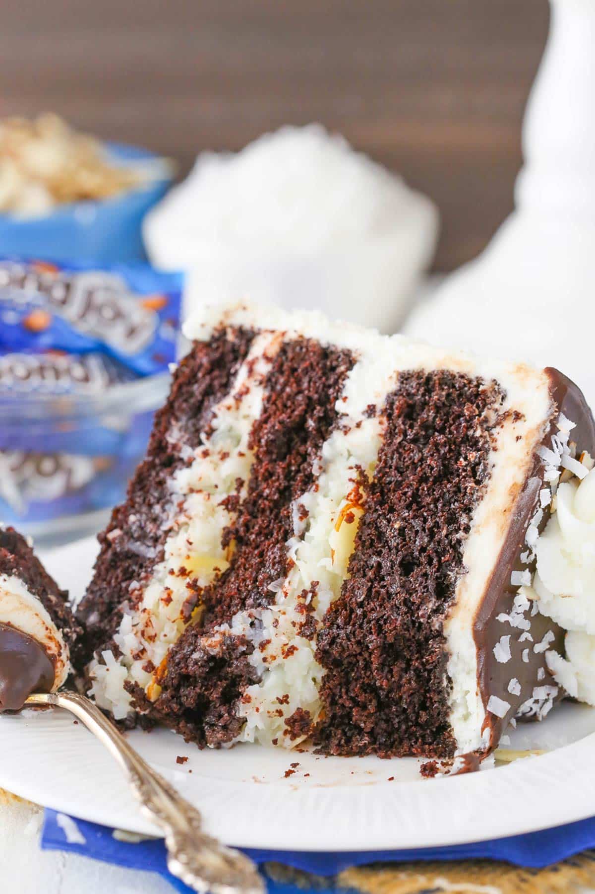 A slice of almond joy layer cake on a plate with a few bites removed.