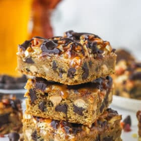 three cookie. bars stacked on top of each other on marble counter with beer and bacon in background