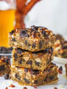 three cookie. bars stacked on top of each other on marble counter with beer and bacon in background
