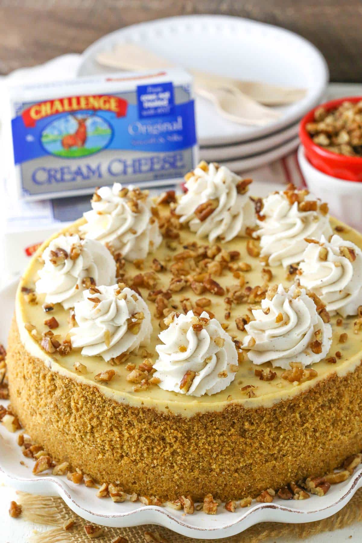 A decorated browned butter pecan cheesecake on a white cake plate.