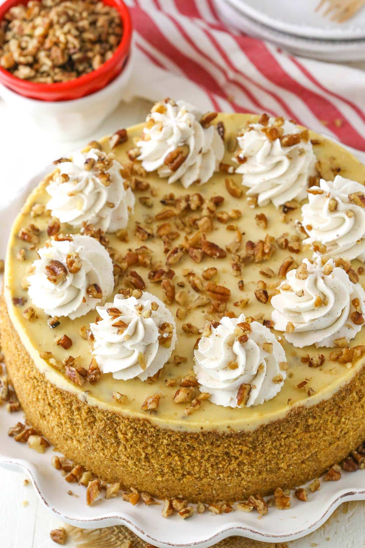 A browned butter pecan cheesecake on a white ruffled cake plate.