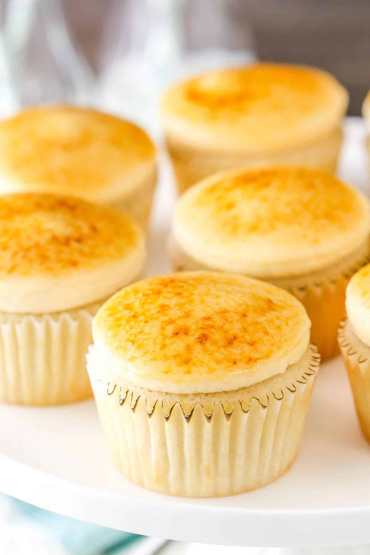 Several creme brulee cupcakes on a white cake plate.
