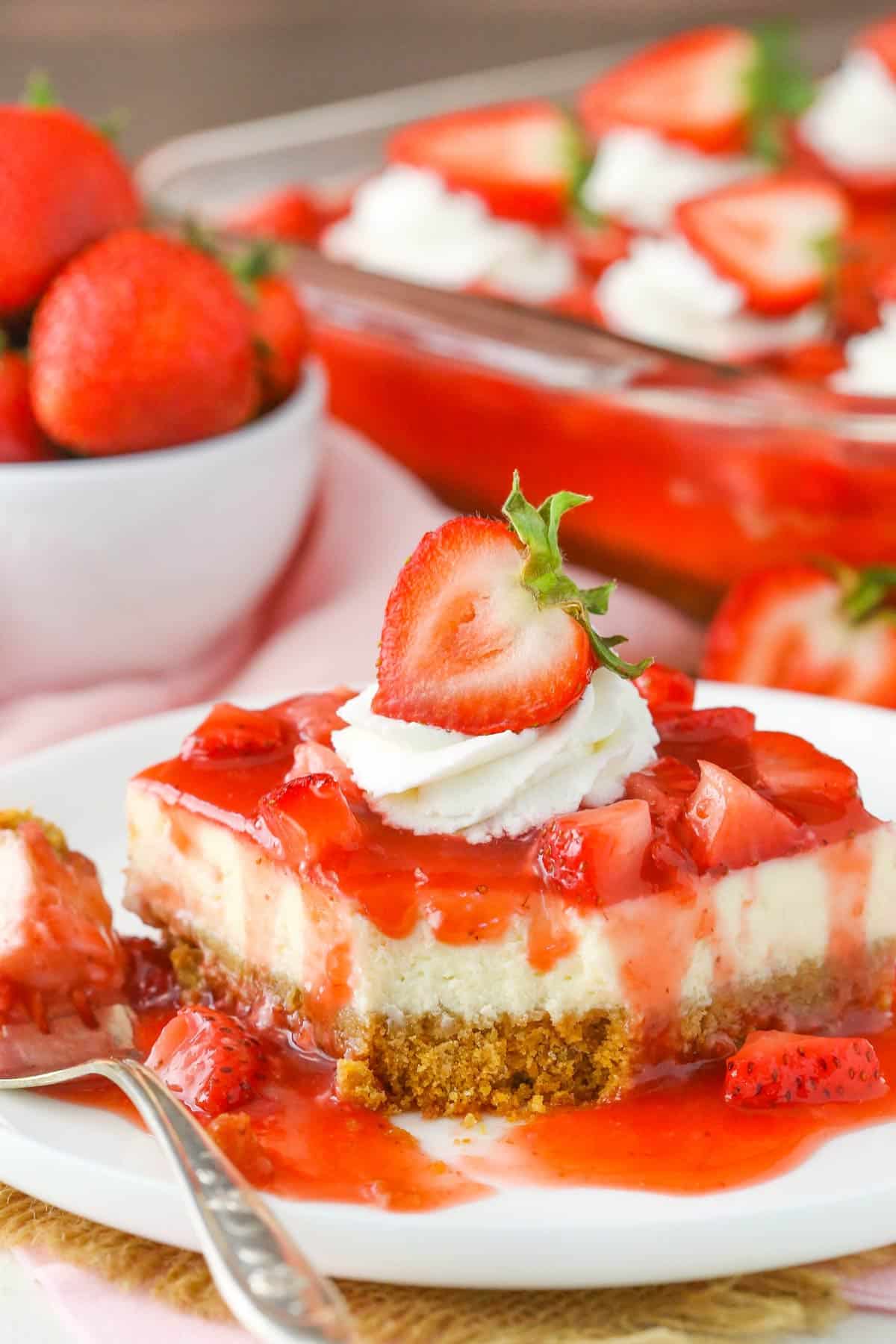 A slice of strawberry cheesecake with a bite removed.