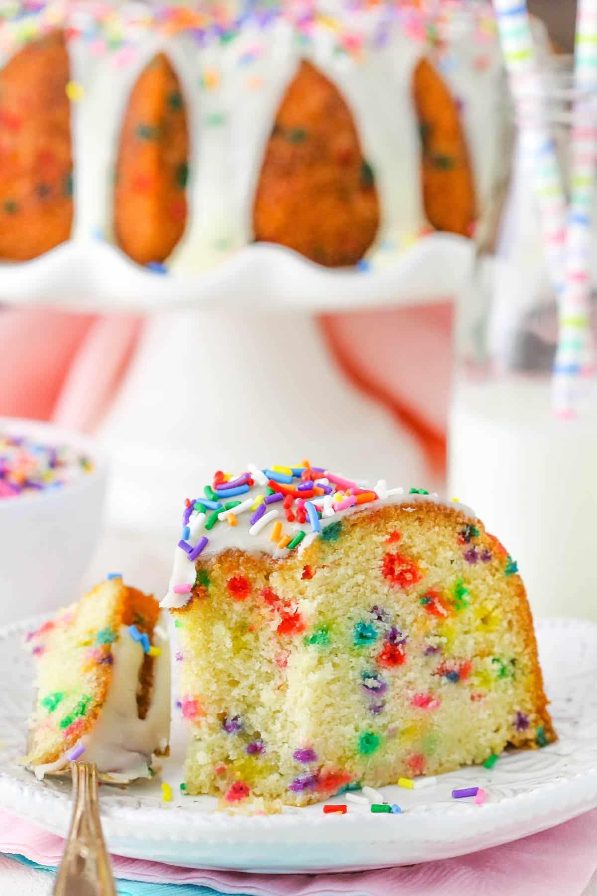 A slice of funfetti bundt cake with a bite removed on a white plate.