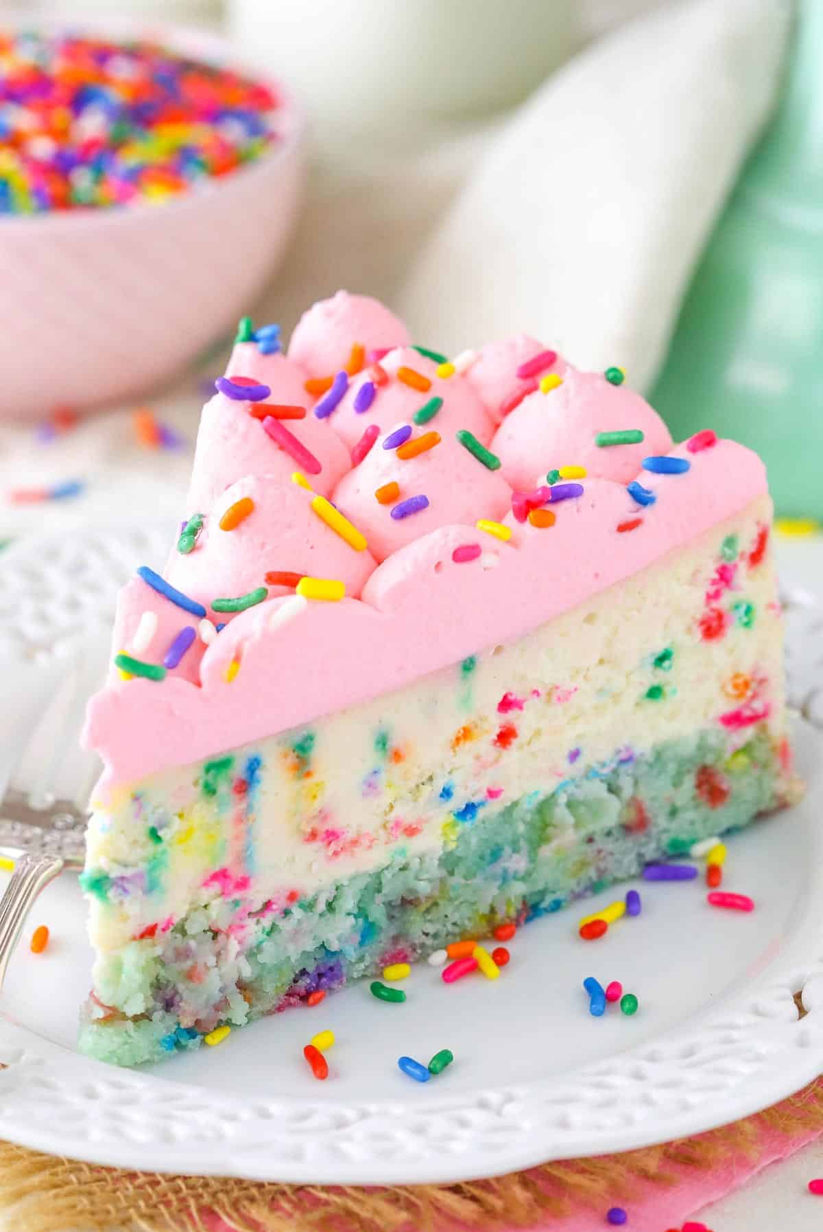 A slice of funfetti cheesecake with cake bottom on a white plate.