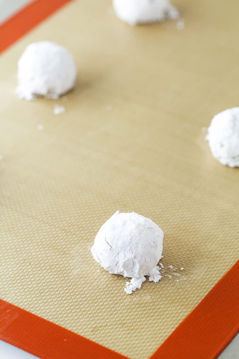 Balls of lemon cookie dough coated in powdered sugar, ready to bake.