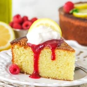A slice of olive oil cake topped with raspberry sauce and whipped cream.