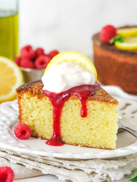 A slice of olive oil cake topped with raspberry sauce and whipped cream.