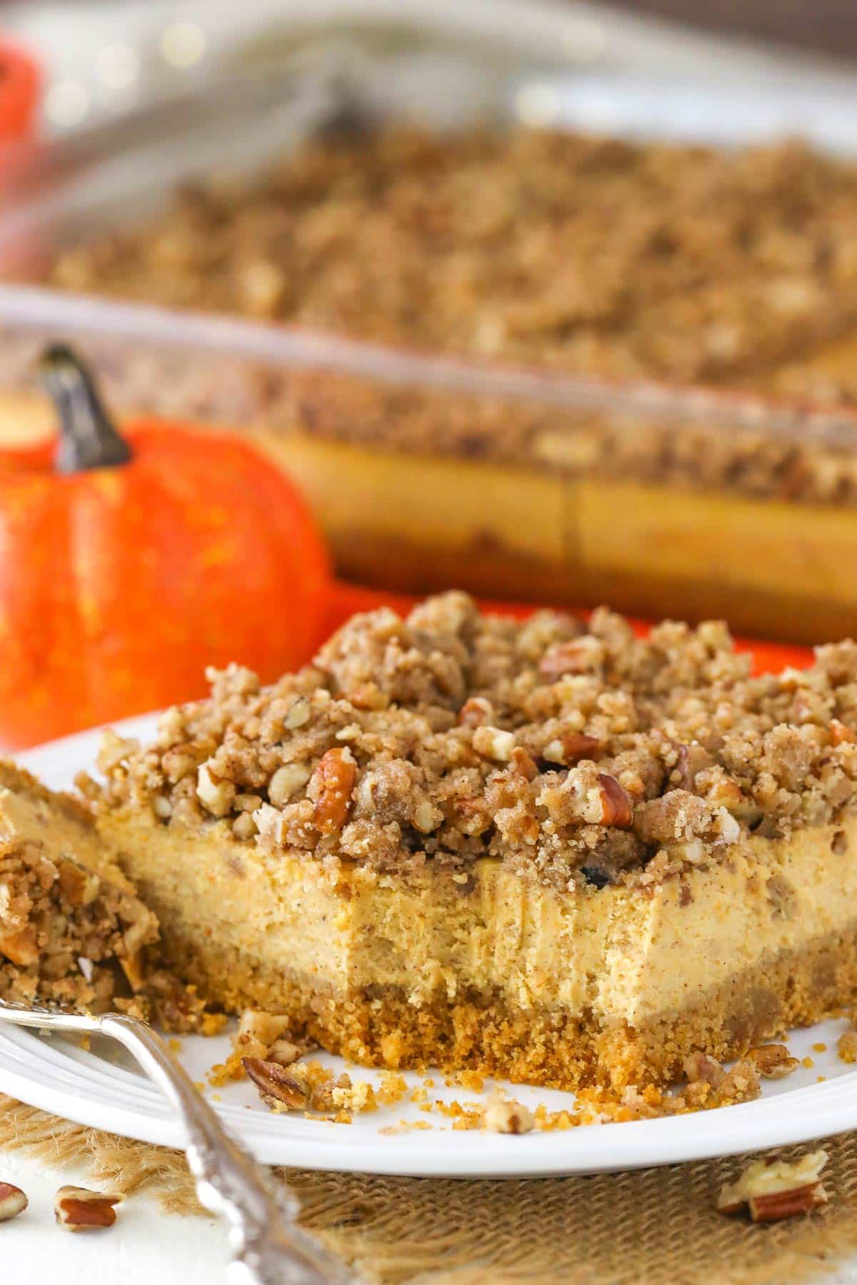 A slice of pecan streusel pumpkin cheesecake with a bite removed on a white plate.
