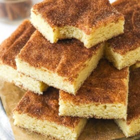 Snickerdoodle cookie bars stacked on a plate. The top bar has a bite taken out of it.